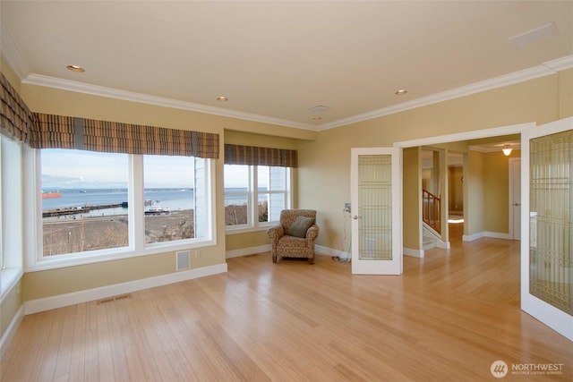 unfurnished room with visible vents, baseboards, ornamental molding, light wood finished floors, and stairs