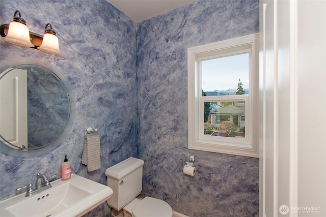 half bath featuring a sink, toilet, and wallpapered walls