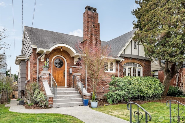 english style home with brick siding, a chimney, a front yard, and roof with shingles