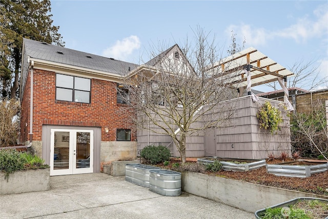 back of house with french doors, a patio, brick siding, and a vegetable garden