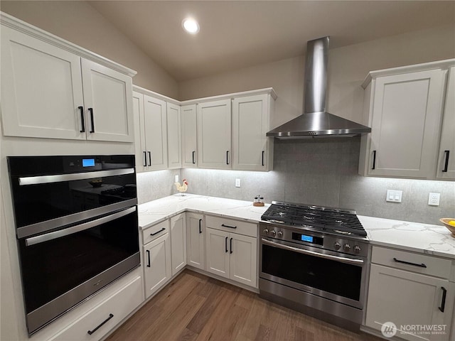 kitchen with wall chimney exhaust hood, light stone counters, wood finished floors, stainless steel appliances, and backsplash