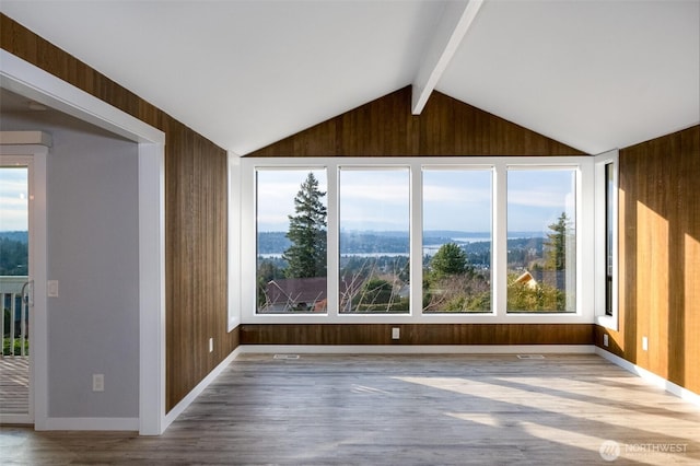 spare room with lofted ceiling with beams, wooden walls, baseboards, and wood finished floors