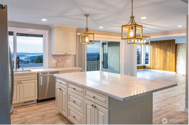 kitchen featuring light wood finished floors, decorative backsplash, dishwasher, cream cabinets, and a sink