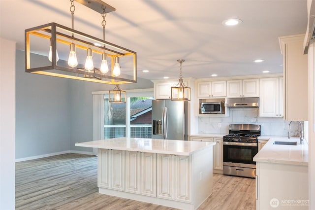 kitchen with under cabinet range hood, stainless steel appliances, a sink, light wood-type flooring, and backsplash