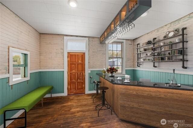 bar with dark wood-type flooring and a wainscoted wall