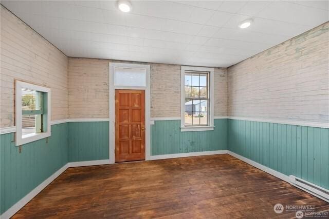 empty room with a wainscoted wall, a baseboard heating unit, and wood finished floors