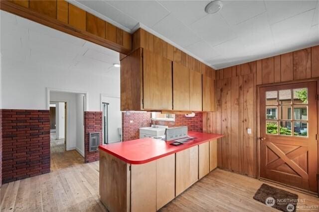 kitchen with light wood-style floors, light countertops, wood walls, and a peninsula