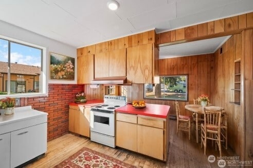 kitchen featuring wooden walls, under cabinet range hood, light wood-style floors, and electric range