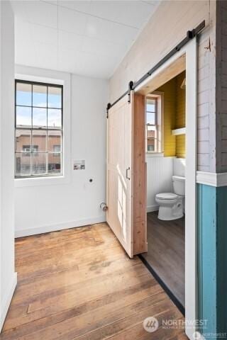 bathroom featuring baseboards, wood finished floors, toilet, and a healthy amount of sunlight