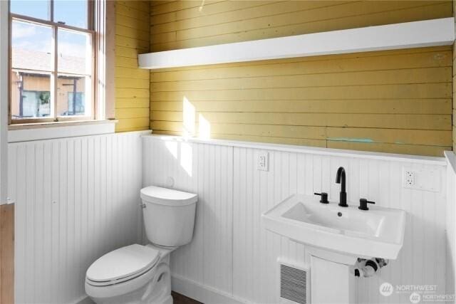 bathroom featuring toilet, a wainscoted wall, visible vents, and a sink