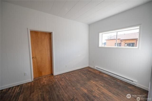 spare room with a baseboard heating unit, baseboards, and hardwood / wood-style flooring