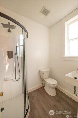 bathroom featuring toilet, wood finished floors, visible vents, baseboards, and a stall shower