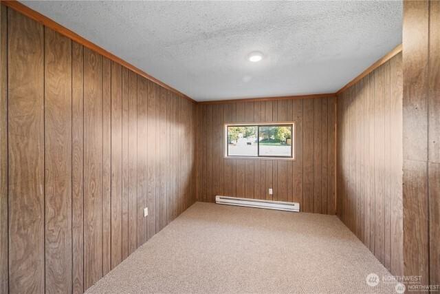 carpeted empty room featuring a baseboard radiator, wood walls, and a textured ceiling