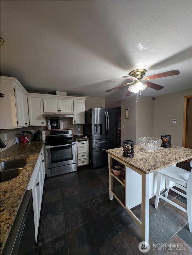 kitchen with light stone counters, appliances with stainless steel finishes, white cabinets, a sink, and a kitchen island