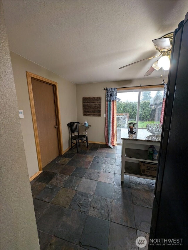 hallway with baseboards, a textured ceiling, and stone tile floors