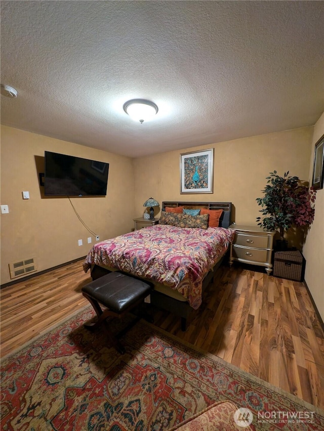 bedroom with a textured ceiling, wood finished floors, and visible vents