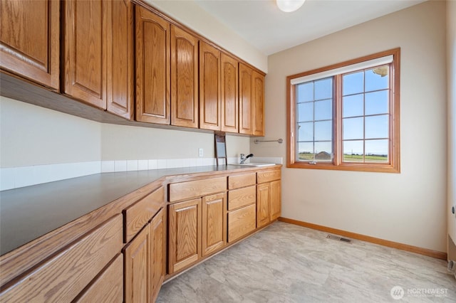 kitchen with brown cabinetry, visible vents, baseboards, and a sink