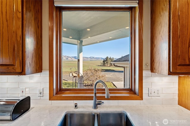 kitchen with brown cabinetry, a mountain view, light stone countertops, and a sink