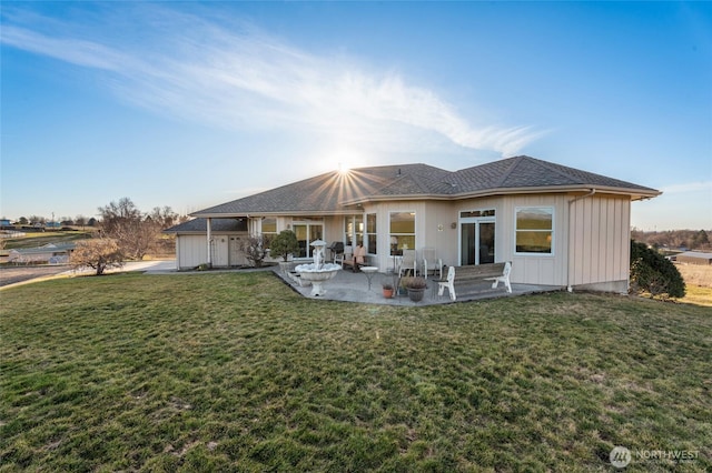 rear view of house featuring a lawn, a shingled roof, and a patio