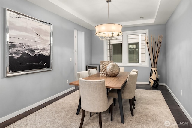 dining space featuring baseboards, visible vents, dark wood-type flooring, a tray ceiling, and a chandelier