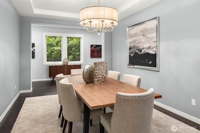 dining room with a chandelier, a raised ceiling, dark wood finished floors, and baseboards