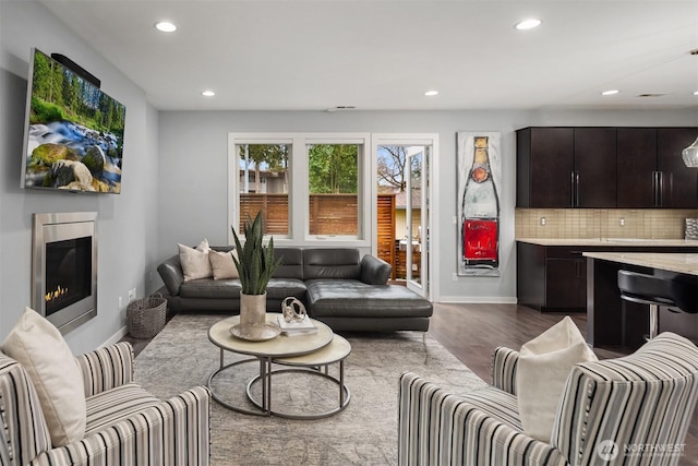 living room with a glass covered fireplace, dark wood finished floors, baseboards, and recessed lighting