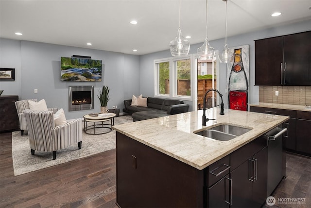 kitchen featuring dark wood-type flooring, a sink, open floor plan, a lit fireplace, and stainless steel dishwasher