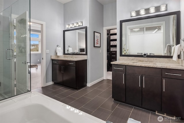 full bathroom featuring two vanities, a bathing tub, a sink, a shower stall, and baseboards