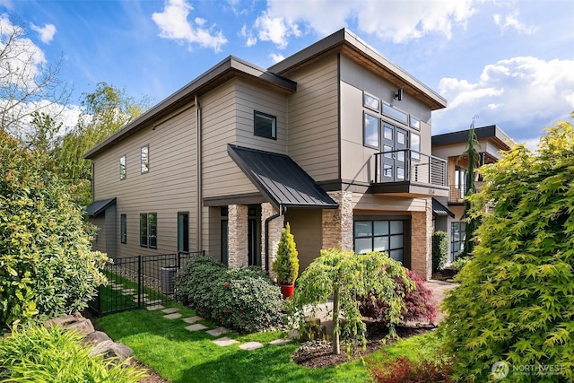 view of front facade with metal roof, a balcony, central AC, stone siding, and a standing seam roof