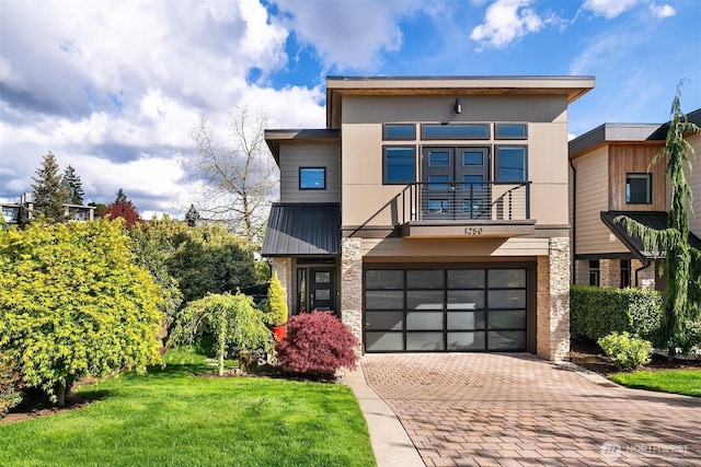 contemporary house featuring a balcony, a garage, decorative driveway, stucco siding, and a front yard