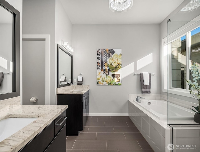 bathroom featuring an inviting chandelier, tile patterned floors, baseboards, two vanities, and a bath