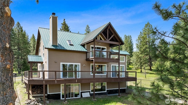 rear view of property featuring a balcony, a chimney, metal roof, and a yard