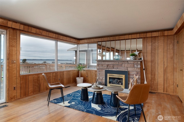 sitting room with a stone fireplace, wooden walls, wood finished floors, and visible vents