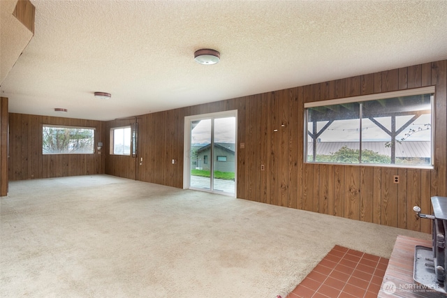 unfurnished living room with carpet flooring, wood walls, a textured ceiling, and a wood stove