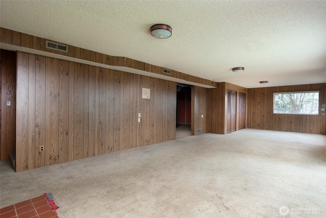 spare room featuring visible vents, carpet, wood walls, and a textured ceiling