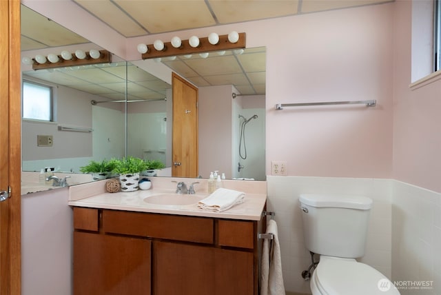 bathroom with vanity, walk in shower, a paneled ceiling, wainscoting, and toilet