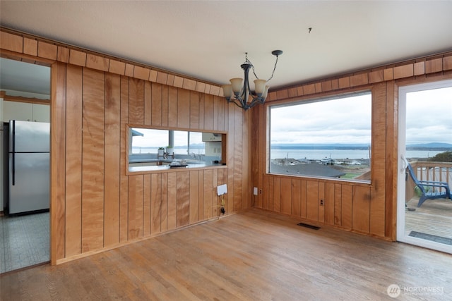 unfurnished dining area with a notable chandelier, a healthy amount of sunlight, visible vents, and light wood-style floors