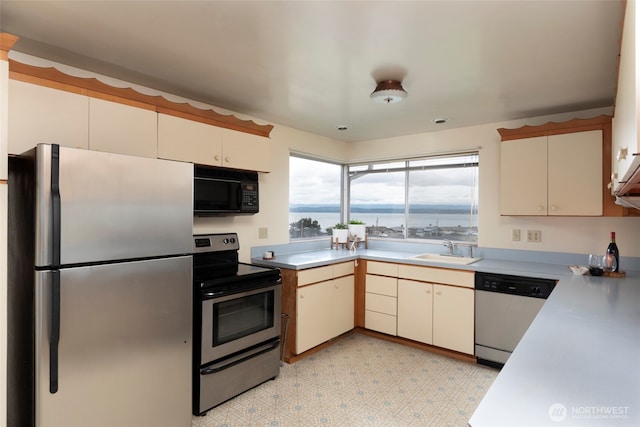 kitchen featuring light floors, a sink, stainless steel appliances, light countertops, and cream cabinets