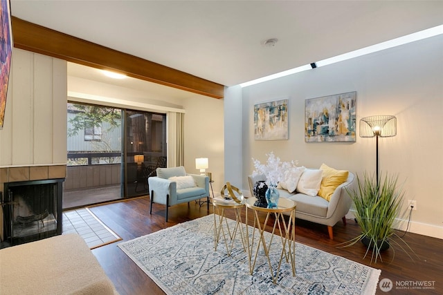 living area with a tiled fireplace, wood finished floors, beam ceiling, and baseboards