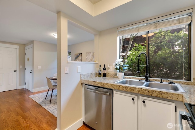 kitchen with light countertops, white cabinets, a sink, wood finished floors, and dishwasher