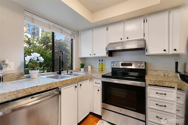 kitchen with under cabinet range hood, stainless steel appliances, a sink, white cabinets, and tile counters