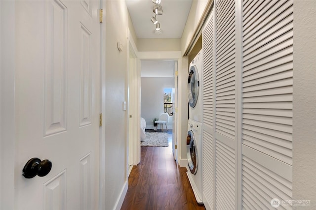 hallway featuring dark wood-style floors, stacked washer / dryer, and baseboards