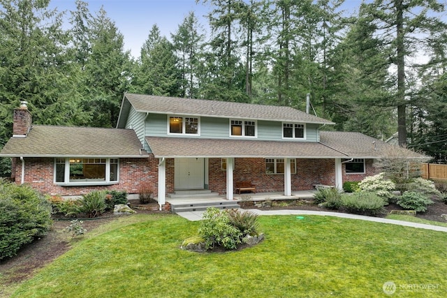 traditional home with a shingled roof, a front yard, and brick siding