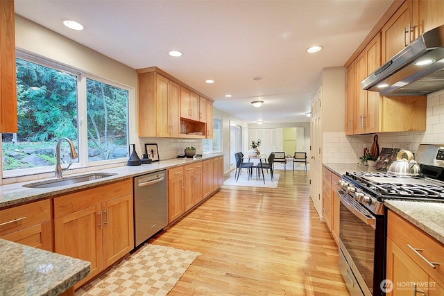 kitchen with light wood-style flooring, under cabinet range hood, a sink, appliances with stainless steel finishes, and light stone countertops