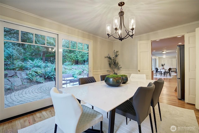 dining area with light wood-type flooring, a chandelier, crown molding, and wainscoting