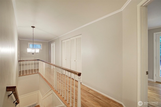 corridor with baseboards, crown molding, an upstairs landing, light wood-style floors, and a chandelier