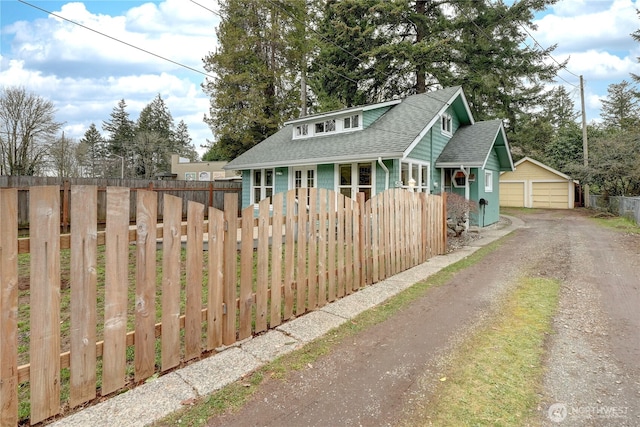 bungalow featuring an outbuilding, covered porch, a shingled roof, a fenced front yard, and a detached garage