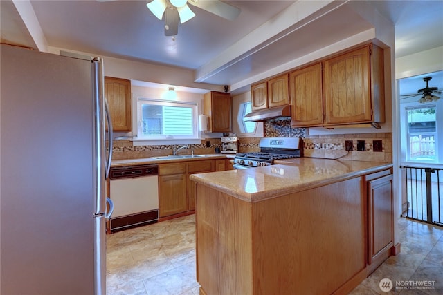 kitchen with a sink, under cabinet range hood, backsplash, appliances with stainless steel finishes, and a peninsula