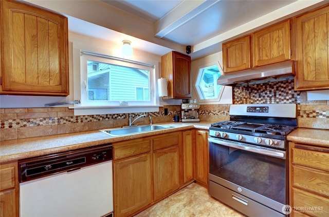 kitchen featuring under cabinet range hood, a sink, white dishwasher, light countertops, and stainless steel gas range