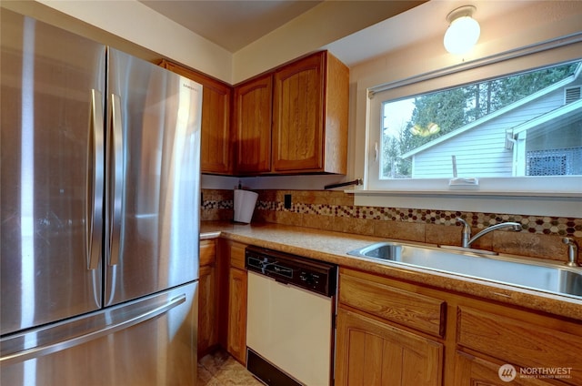 kitchen with a sink, freestanding refrigerator, brown cabinetry, light countertops, and dishwasher